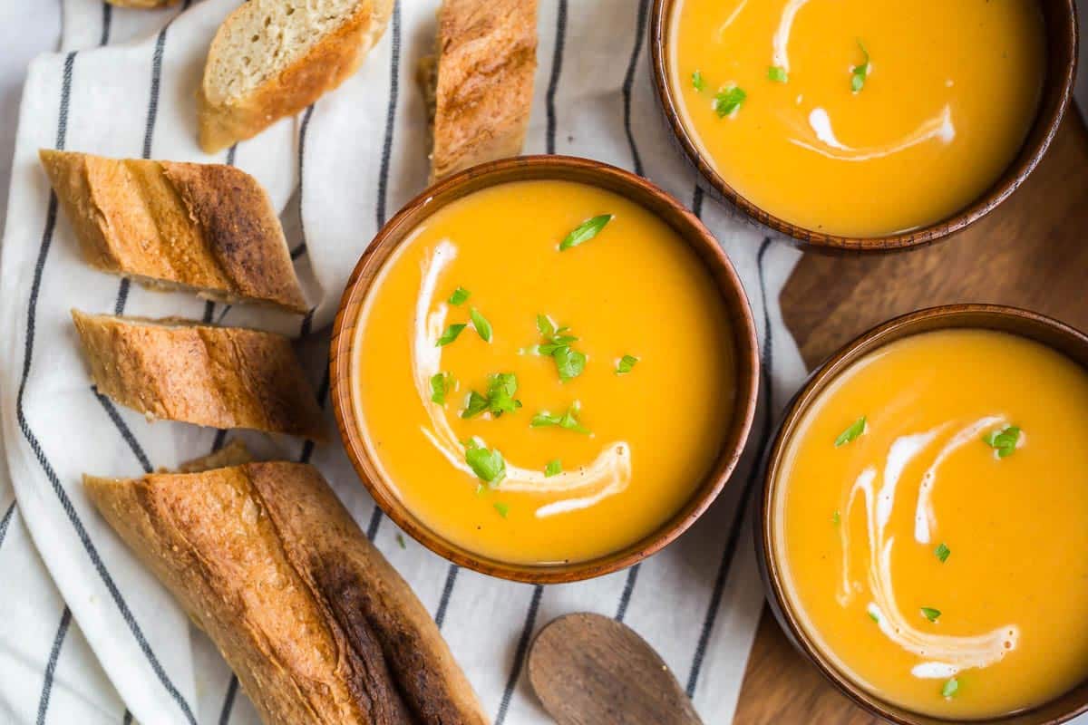 Three wooden bowls with creamy butternut squash soup and a drizzle of cream and sprinkle of parsley.