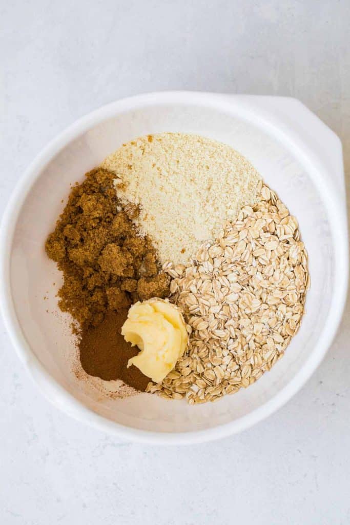 white bowl with oats, almond flour, butter, brown sugar and spices.