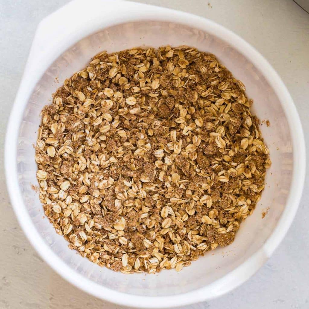 white bowl with oats mixed together with almond flour, butter, brown sugar and spices.