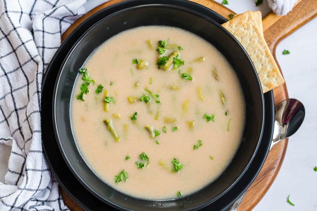 asparagus soup in black bowl on top of wooden platter.