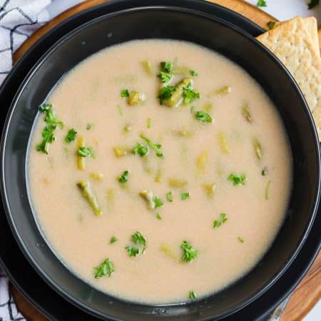 asparagus soup in black bowl on top of wooden platter.