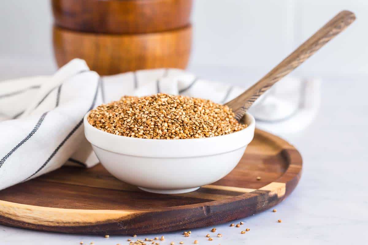 White bowl of crispy quinoa with wooden spoon on a wood plate.