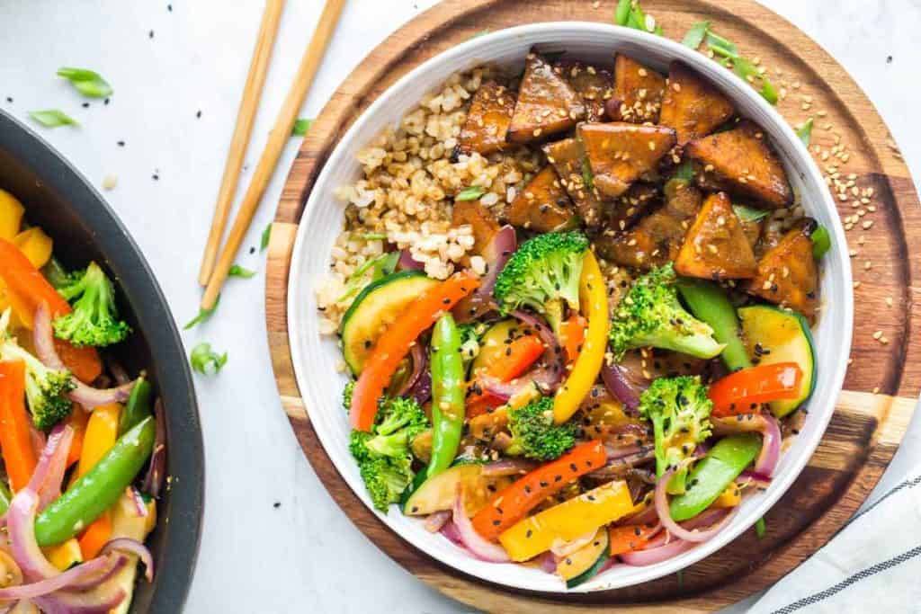 Teriyaki tofu stir fry bowls with coconut rice in a white bowl on a wooden cutting board