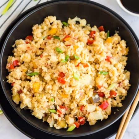 Healthy Cauliflower Fried Rice in a black bowl with chop sticks