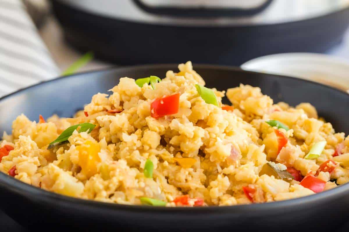 A black matte bowl full of cooked Cauliflower Fried Rice. 