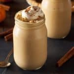 dark background with pumpkin milkshake in a glass mason jar. Shake has whipped cream and cinnamon decoration on top.