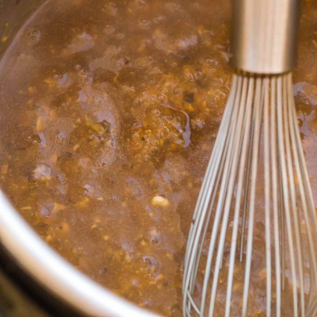 gravy being cooked and stirred in an instant pot with a wire whisk