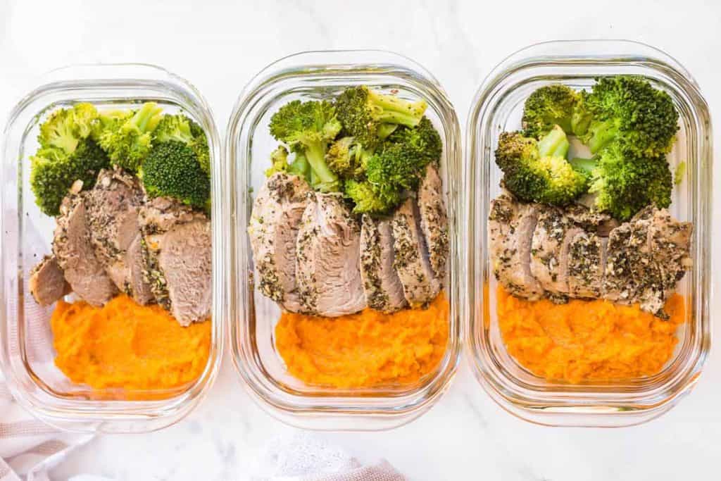three meal prep containers full of mashed sweet potatoes, broccoli and pork