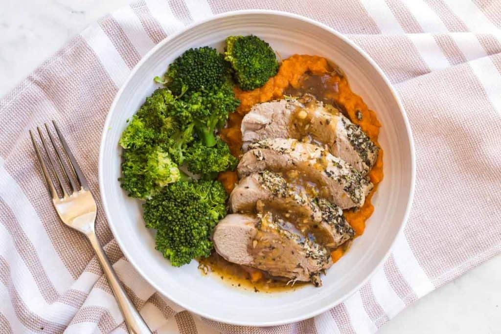 white plate with cooked pork and gravy with mashed sweet potatoes and broccoli