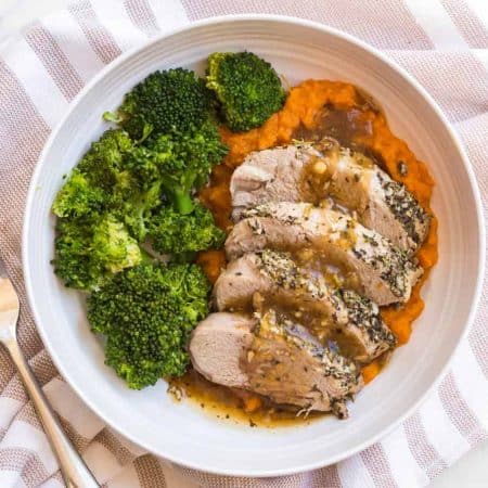 white plate with cooked pork and gravy with mashed sweet potatoes and broccoli