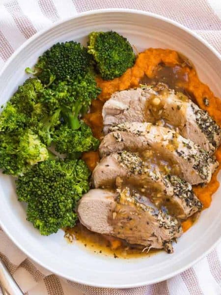 white plate with cooked pork and gravy with mashed sweet potatoes and broccoli