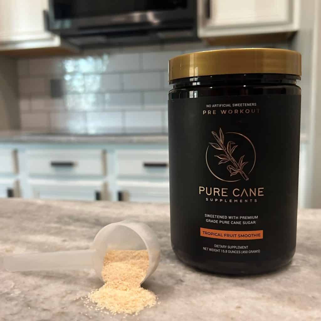 close up of pure cane pre workout powder on a marble counter. One scoop of powder is lying sideways on the counter with powder pouring out.