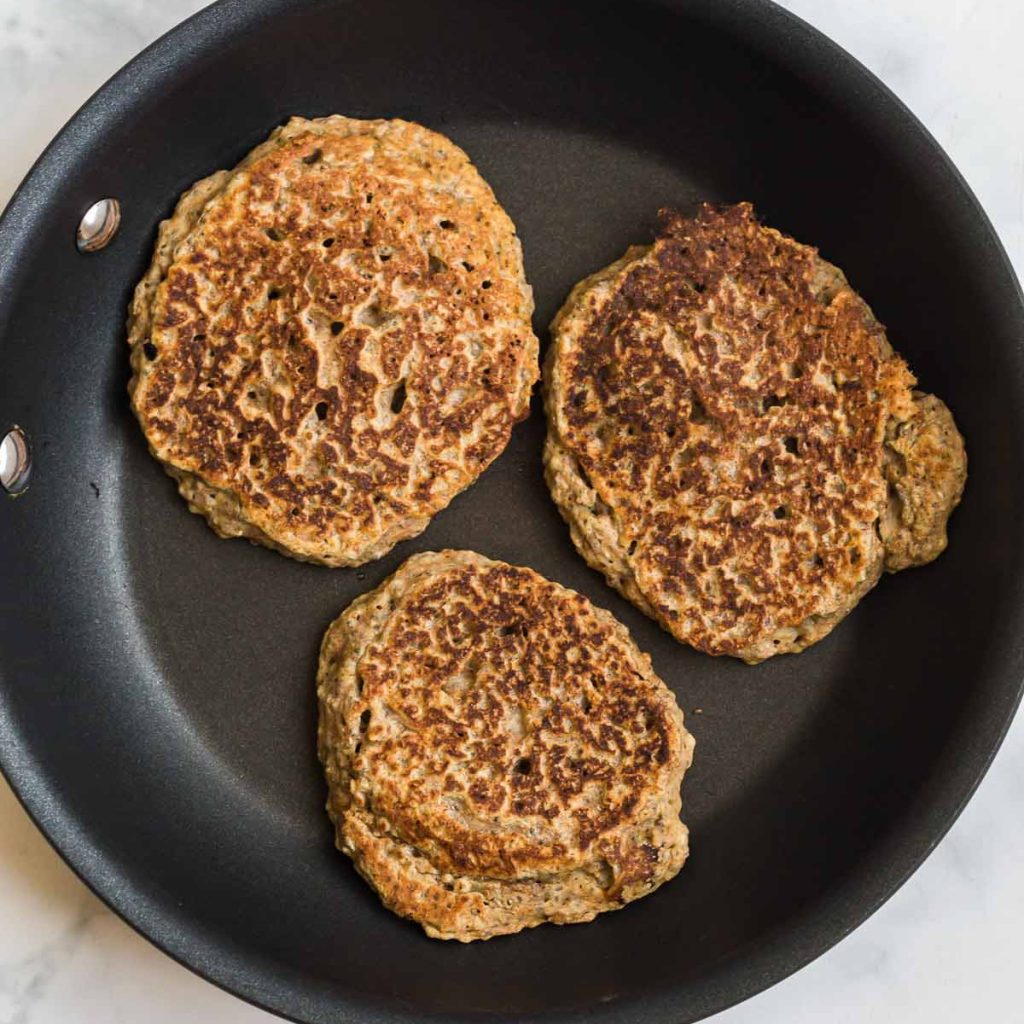 black skillet with three vegan whole wheat pancakes being cooked