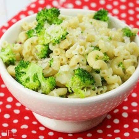 white bowl full of pasta, broccoli and parmesan on top of a red and white tablecloth