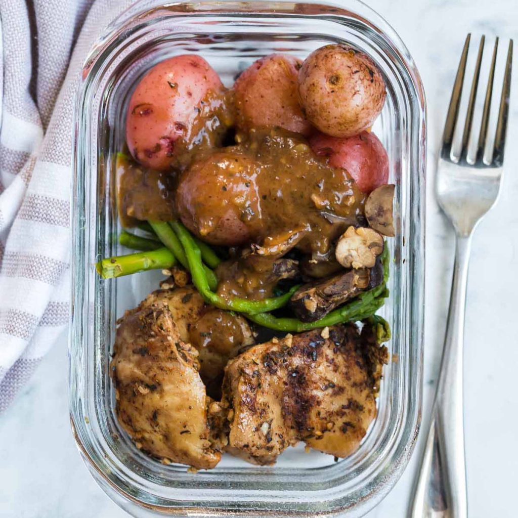 glass meal prep container with potatoes, asparagus, chicken thighs and sauce.