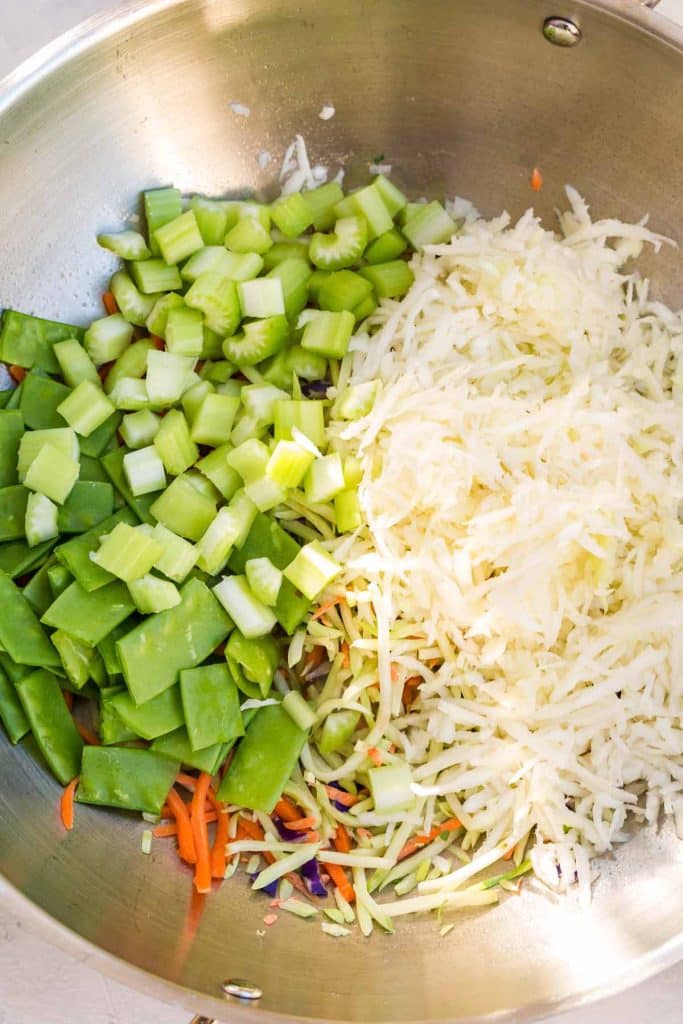 stainless pan with garlic, ginger, cabbage, carrots, broccoli slaw, celery, and snow peas and other ingredients for vegetable lo mein