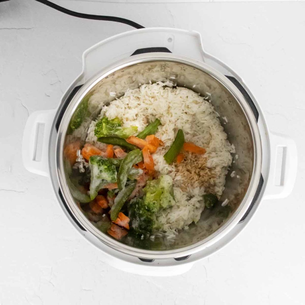 cooked white rice in the instant pot and frozen vegetables on the other side of the pot.