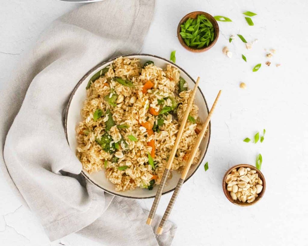 top down view of vegetable fried rice on a white counter with chopsticks resting on the right side of the bowl