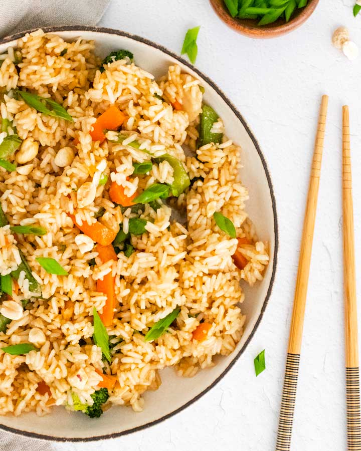 cooked vegetable fried rice in a white bowl with chopsticks to the right side