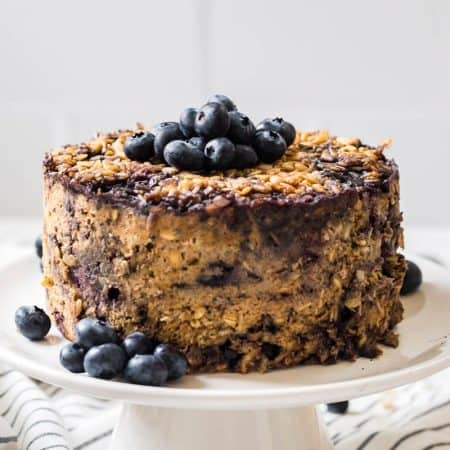 baked oatmeal on cake stand topped with fresh blueberries