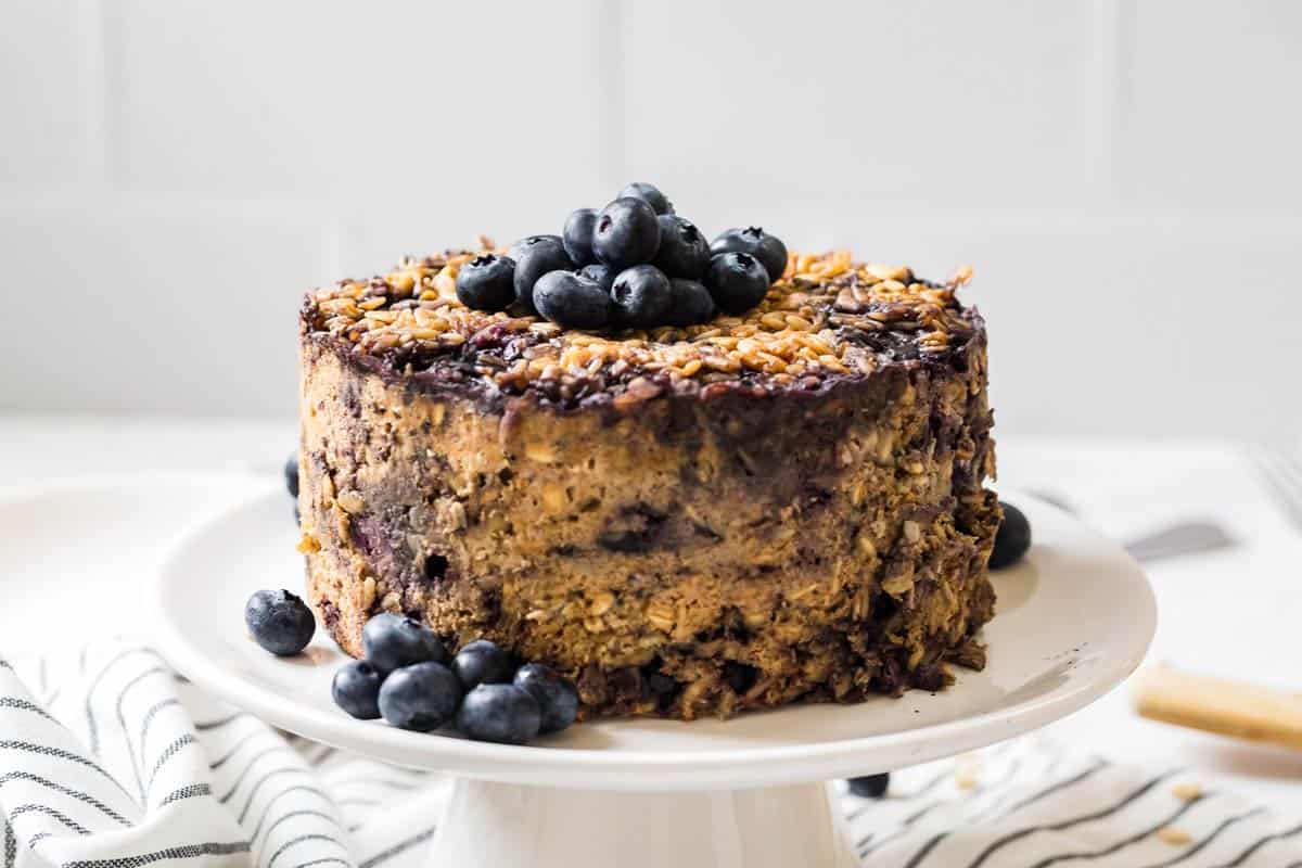 Baked oatmeal on a white cake stand topped with fresh blueberries.