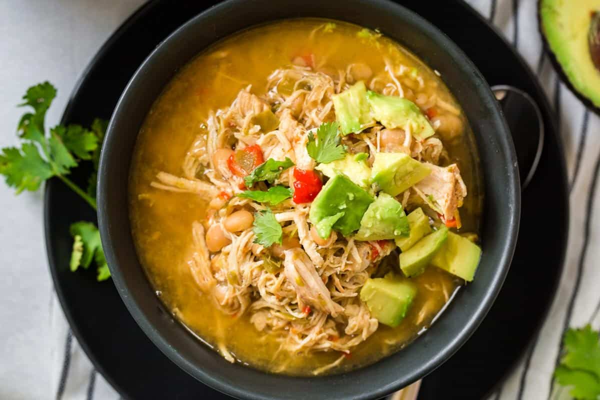 black bowl on top filled with white chicken chili and topped with avocado and cilantro.