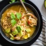 Black and white striped napkin with black bowl on top filled with white chicken chili and topped with avocado and cilantro.