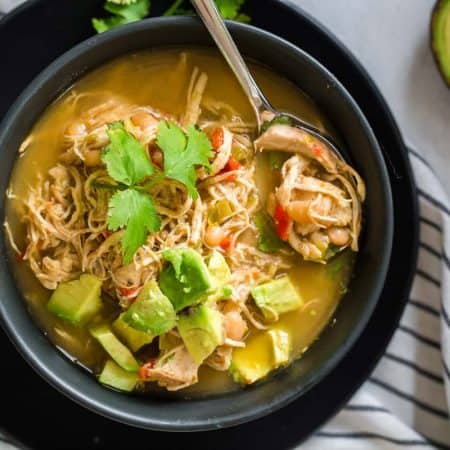 black and white striped napkin with black bowl on top filled with white chicken chili and topped with avocado and cilantro.