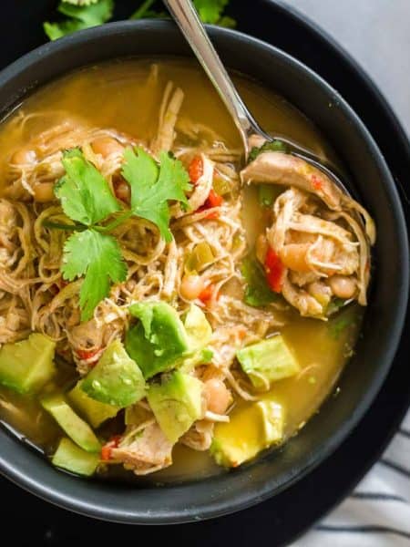 black and white striped napkin with black bowl on top filled with white chicken chili and topped with avocado and cilantro.