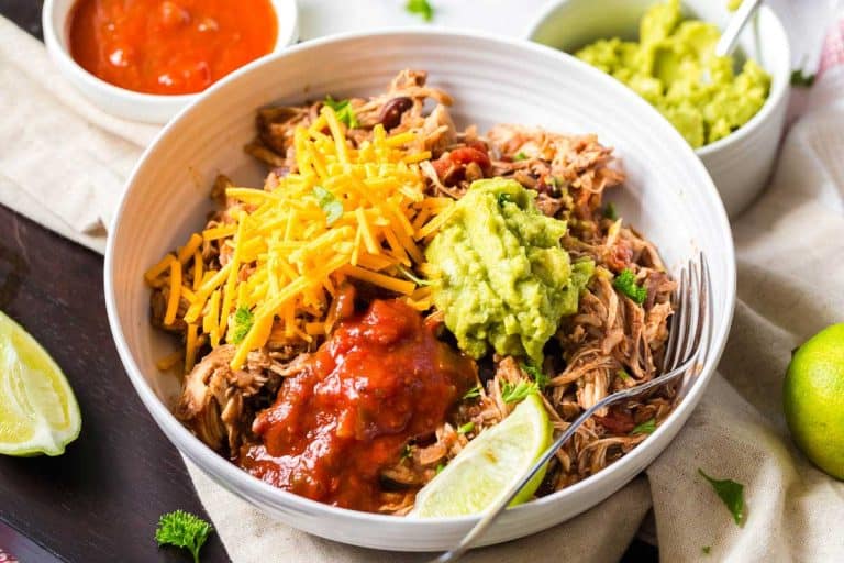 white bowl on top of linen napkin. Bowl has shredded chicken, salsa, cheese, guacamole and a lime wedge inside.