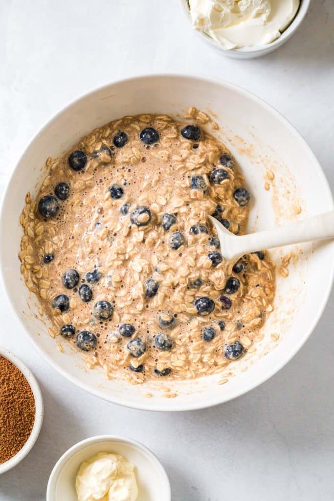 white mixing bowl with wet ingredients and fresh blueberries to make Blueberry Oatmeal Bake