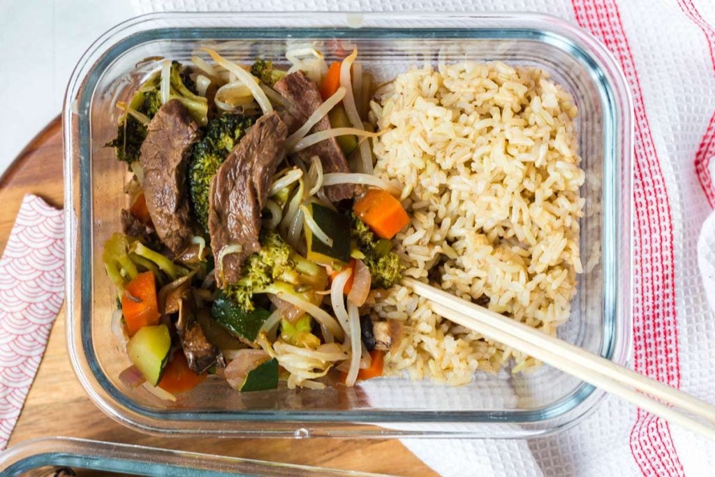 close up of glass container with beef and vegetables with cooked brown rice