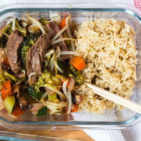 close up of glass container with beef and vegetables with cooked brown rice