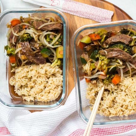 two glass meal prep containers with beef stir fry and cooked brown rice