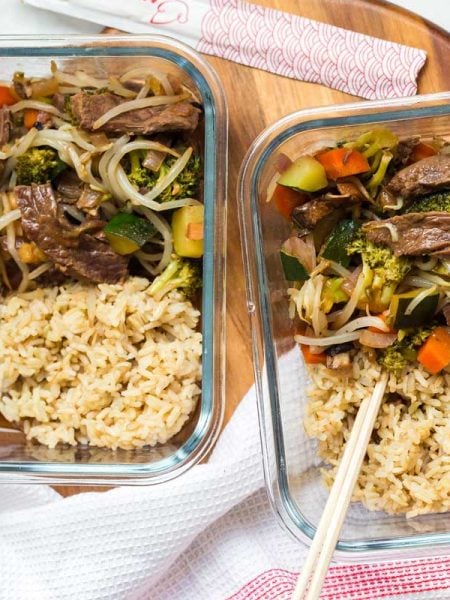 two glass meal prep containers with beef stir fry and cooked brown rice