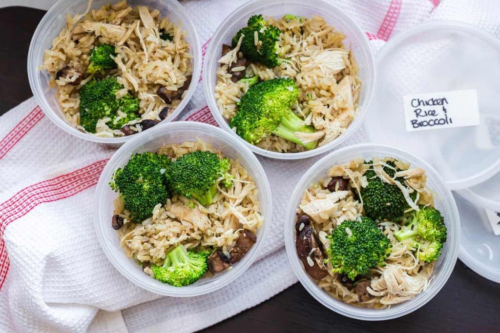 four containers with rice and chicken and broccoli shown from above