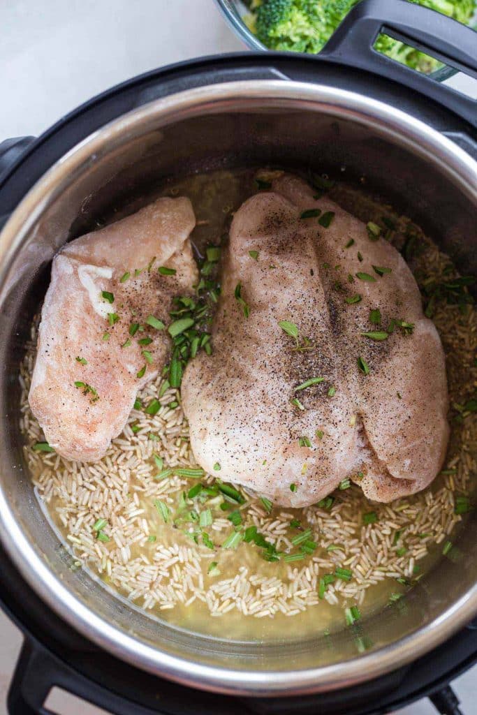 top down view of inside of Instant Pot, containing brown rice, broth, and chicken breast