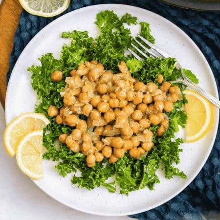 white plate with lemon slices and a bed of kale topped with chickpea salad