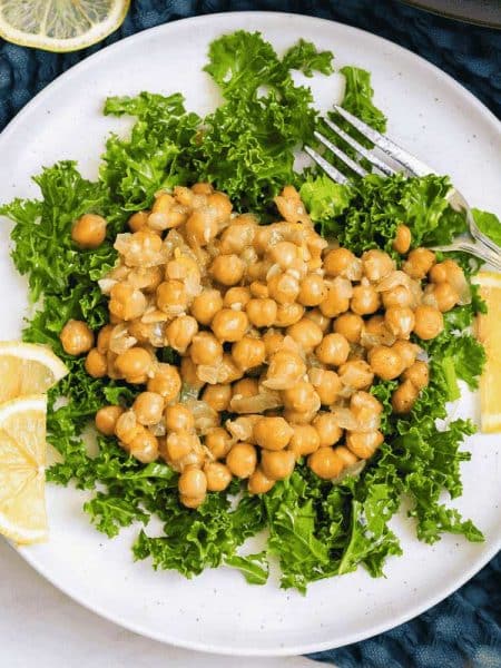white plate with lemon slices and a bed of kale topped with chickpea salad