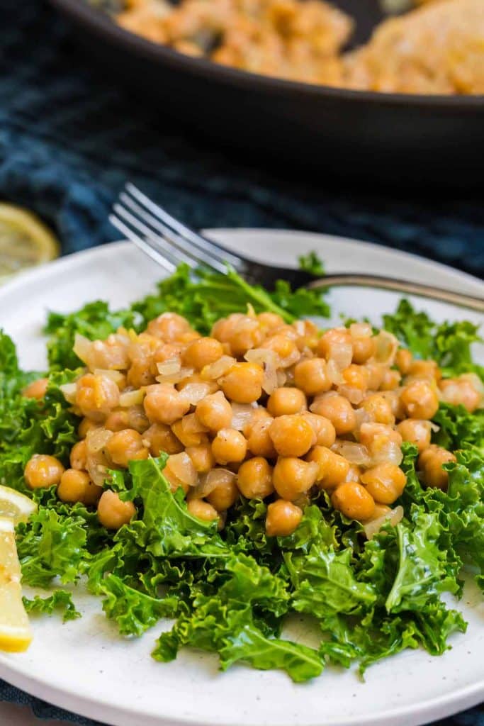 kale salad with cooked chickpeas on top on a white plate