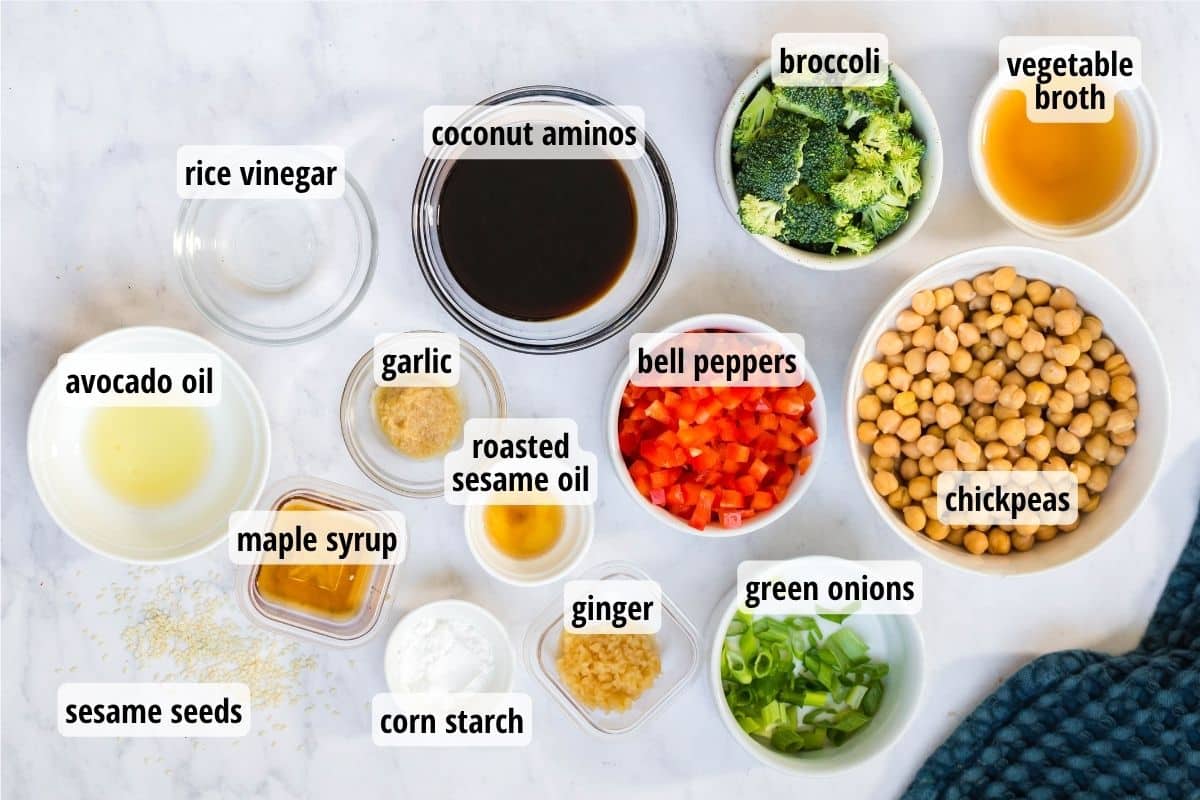 A white marbled counter top with a variety of bowls, all labeled, full of different ingredients that are needed to make Sweet and Sticky Sesame Chickpeas & Veggies.