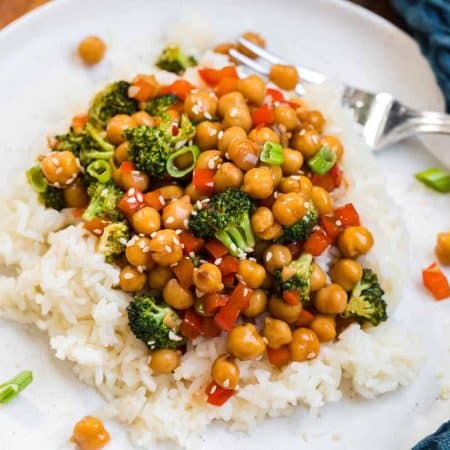 Cooked sweet and sticky sesame chickpeas on a white plate. There is a fork on the right side of the plate and a blue napkin in the background.