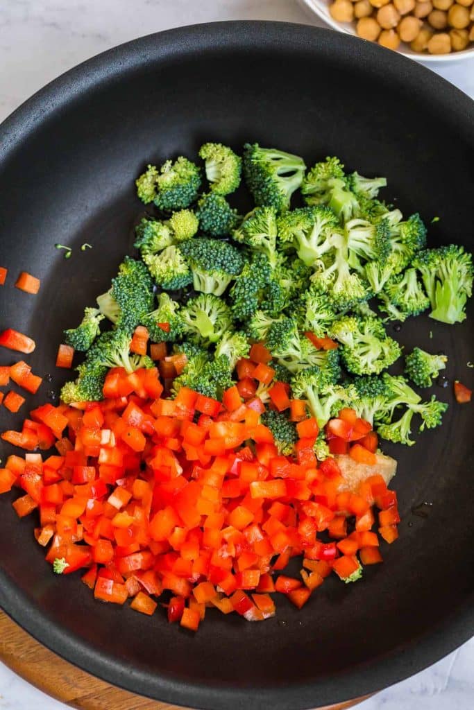 cast iron pan with diced broccoli and red peppers cooking