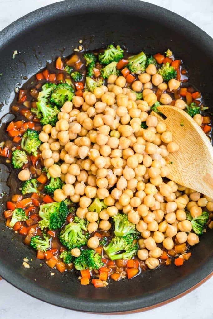 cast iron pan with wooden spoon mixing broccoli, red pepper, and chickpeas.