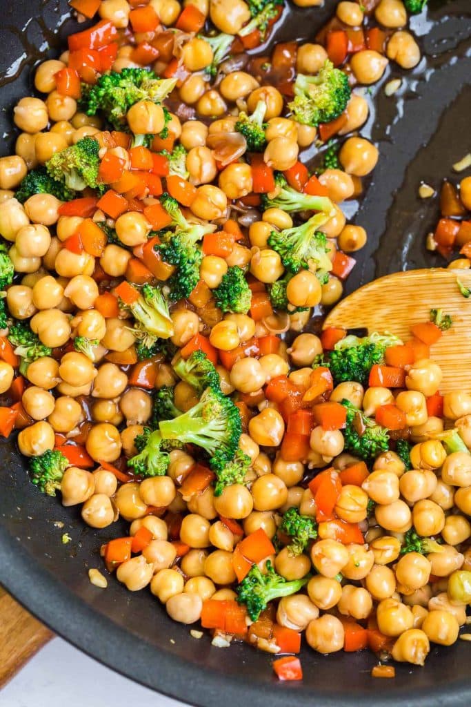 cast iron pan with wooden spoon mixing broccoli, red pepper, and chickpeas.