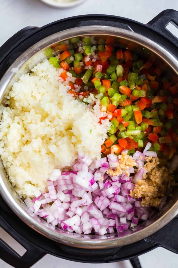 ingredients including diced bell peppers, onions, riced cauliflower and garlic inside of an instant pot