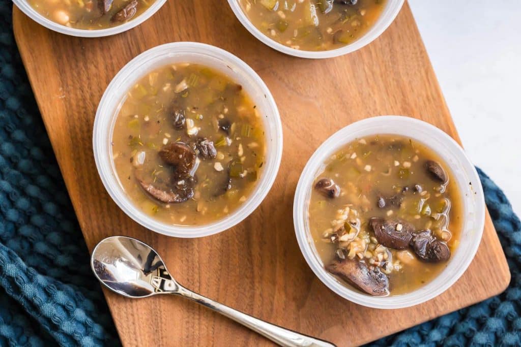 image of two meal prep bowls with soup on top of a wooden board with a spoon