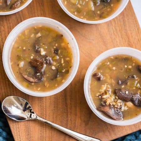 image of two meal prep bowls with soup on top of a wooden board with a spoon