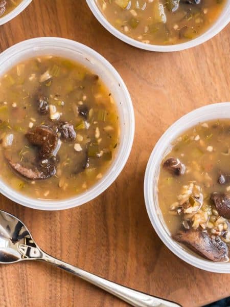 image of two meal prep bowls with soup on top of a wooden board with a spoon