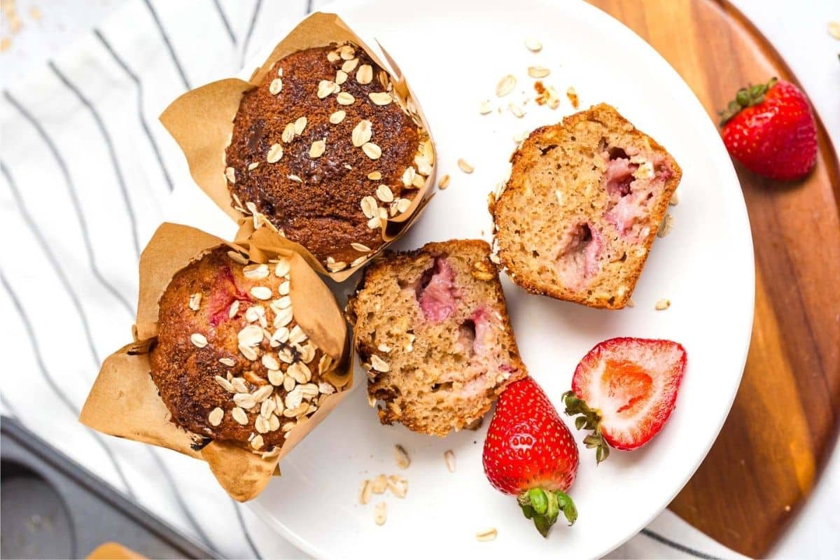 A white plate with 3 strawberry muffins, one is cut in half, on top. 